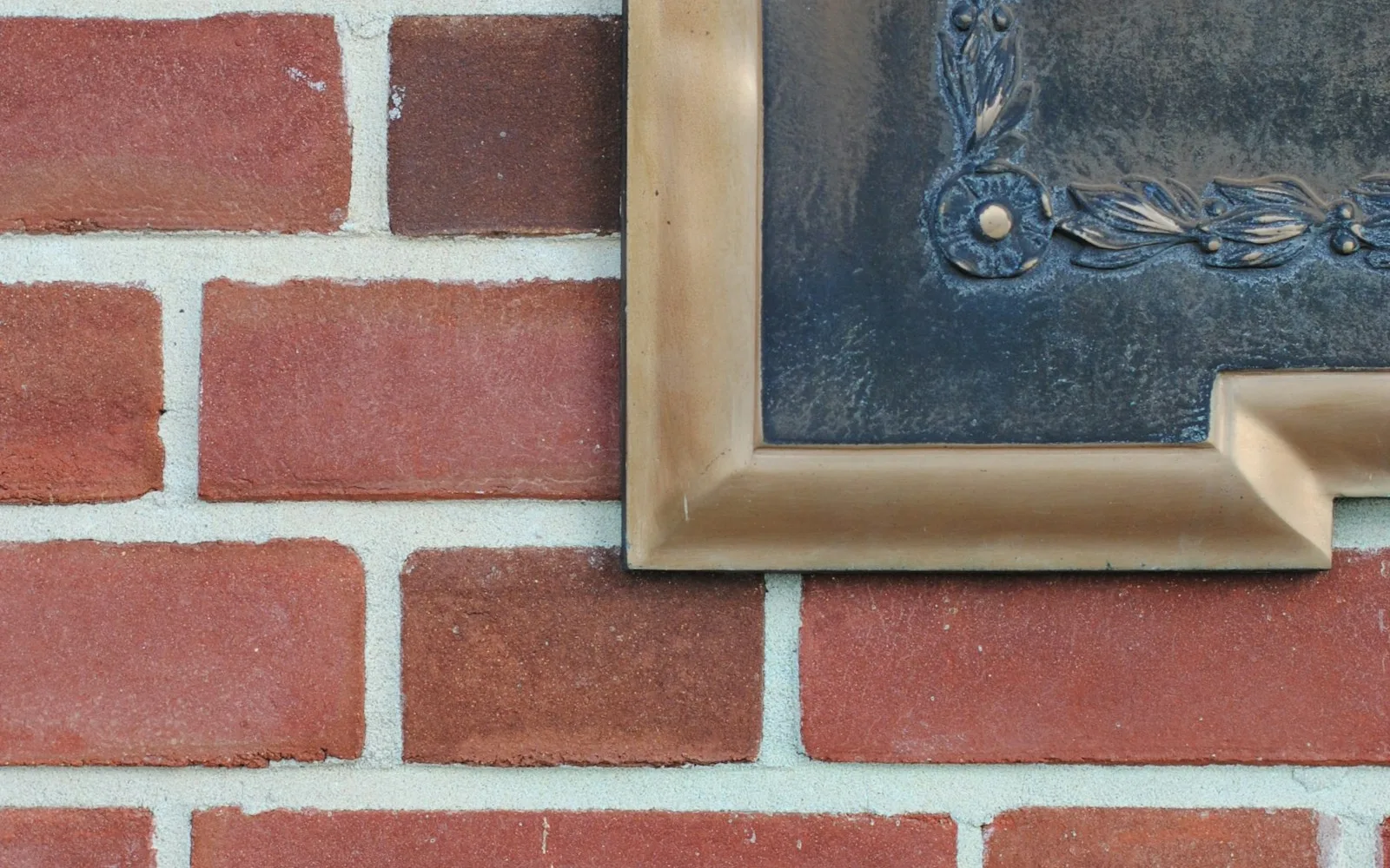 Angolo di una targa con cornice in ottone fissata su un muro di mattoni.
