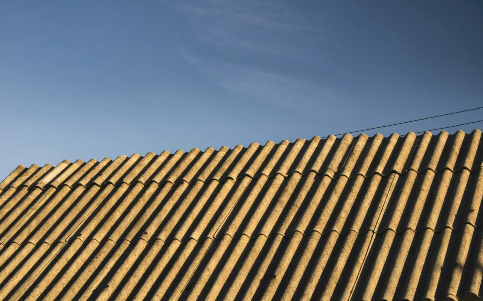 Copertura in lastre ondulate di cemento-amianto su un edificio, vista dal basso contro il cielo.
