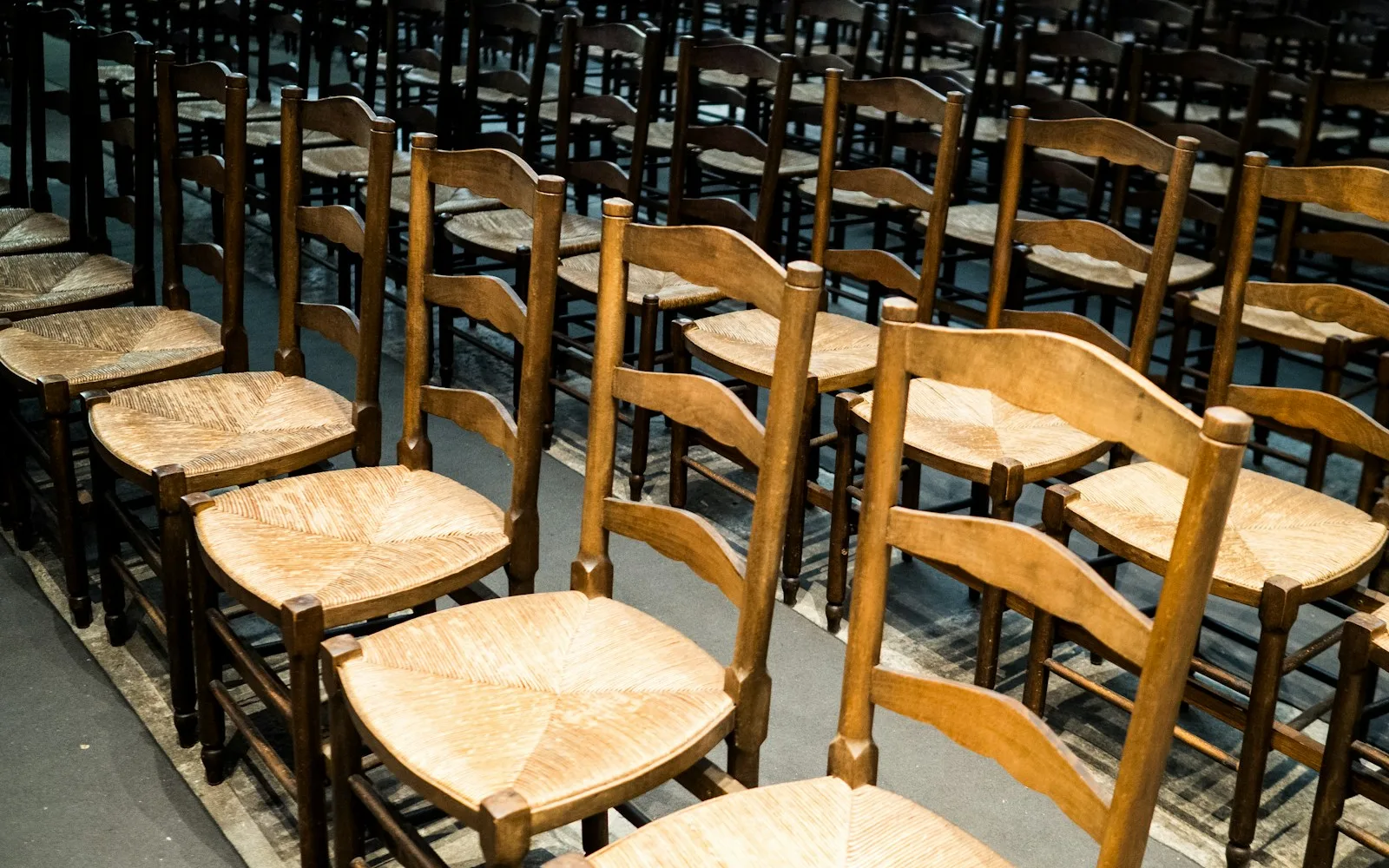 File di sedie in legno con seduta impagliata disposte in una sala prima di una riunione.