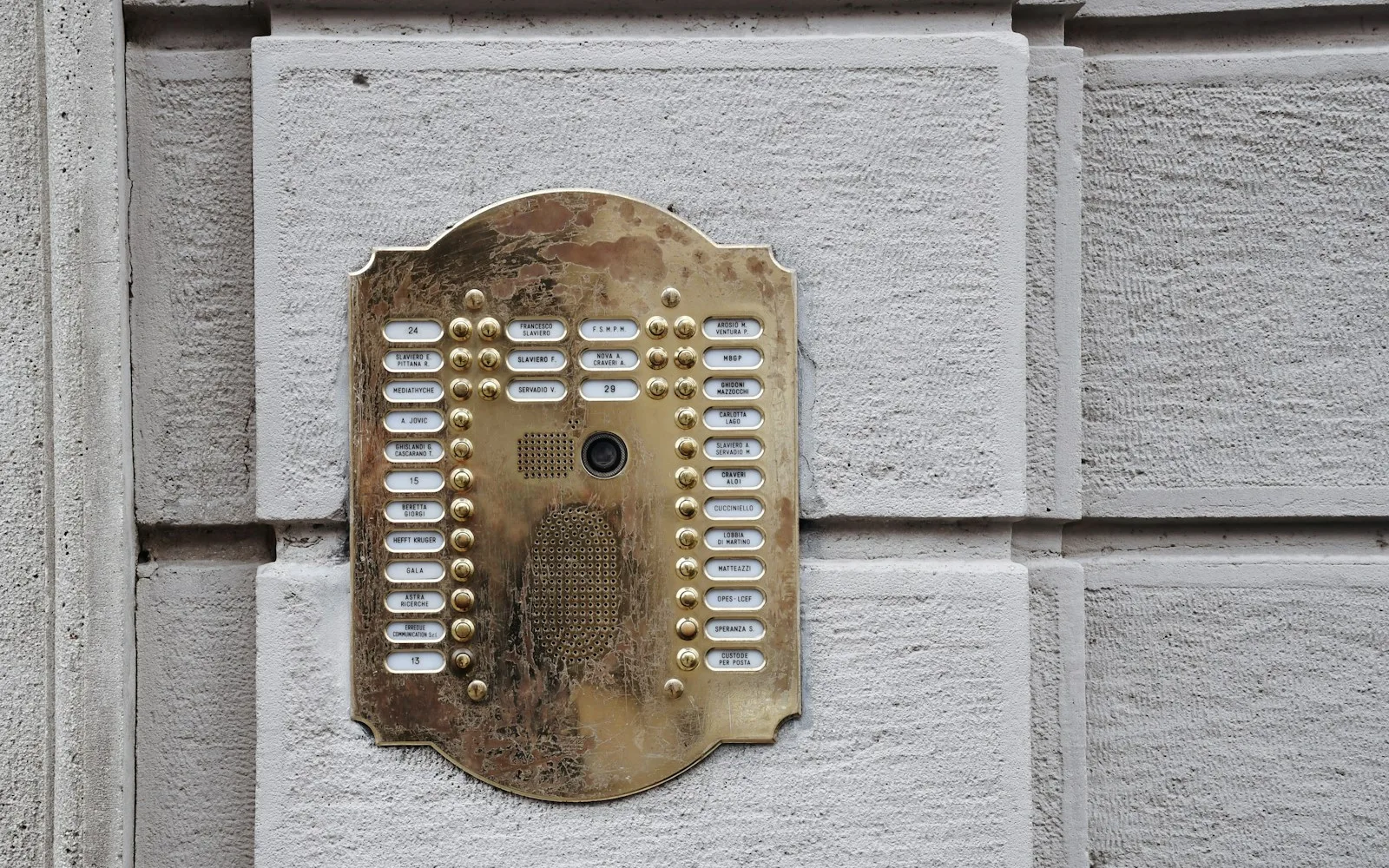 Pulsantiera di ottone di un palazzo italiano con targhette che alternano cognomi di famiglie e nomi di studi e societa.