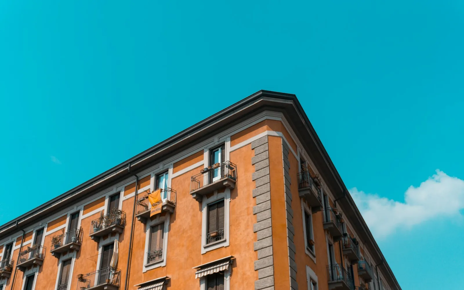 Palazzo d'angolo italiano con intonaco color terracotta, balconcini in ferro battuto e tende da sole.