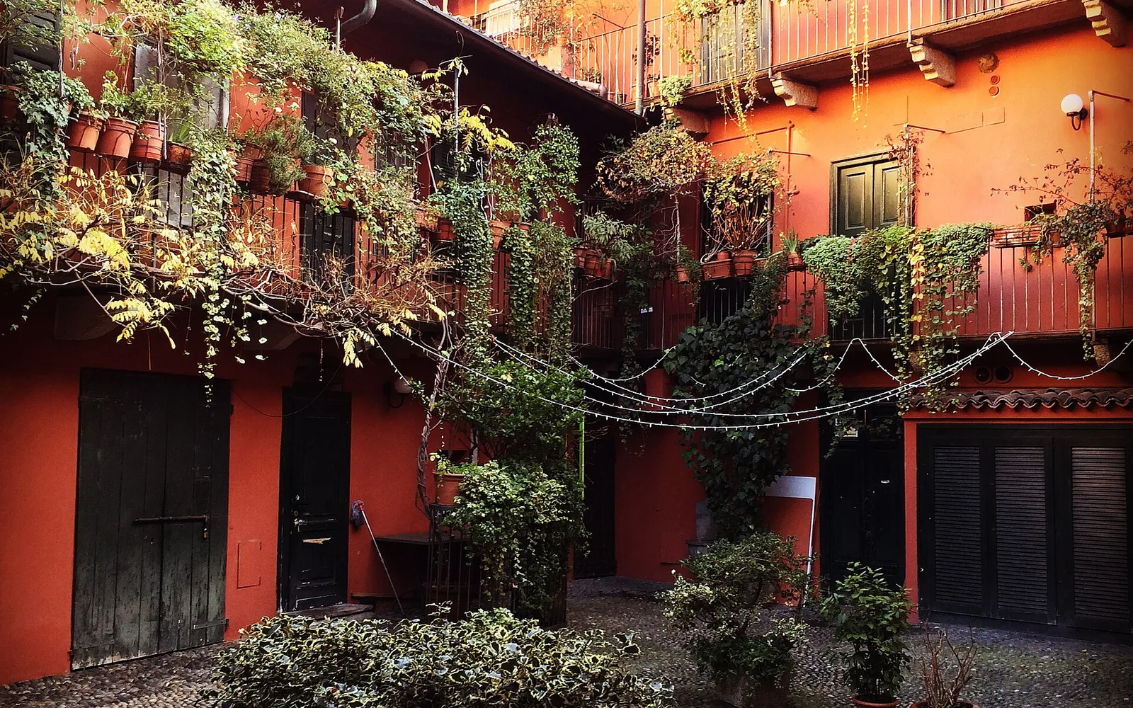 Cortile di una casa di ringhiera a Milano con ballatoi, ringhiere in ferro e piante.