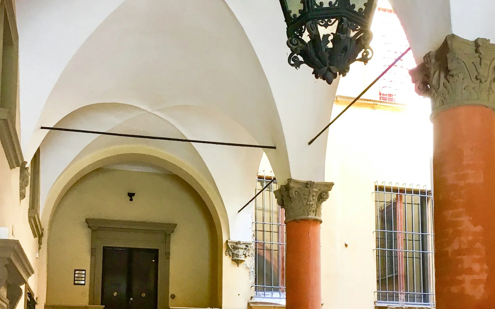 Androne voltato di un palazzo italiano con lanterna in ferro battuto e scalinata con tappeto rosso.