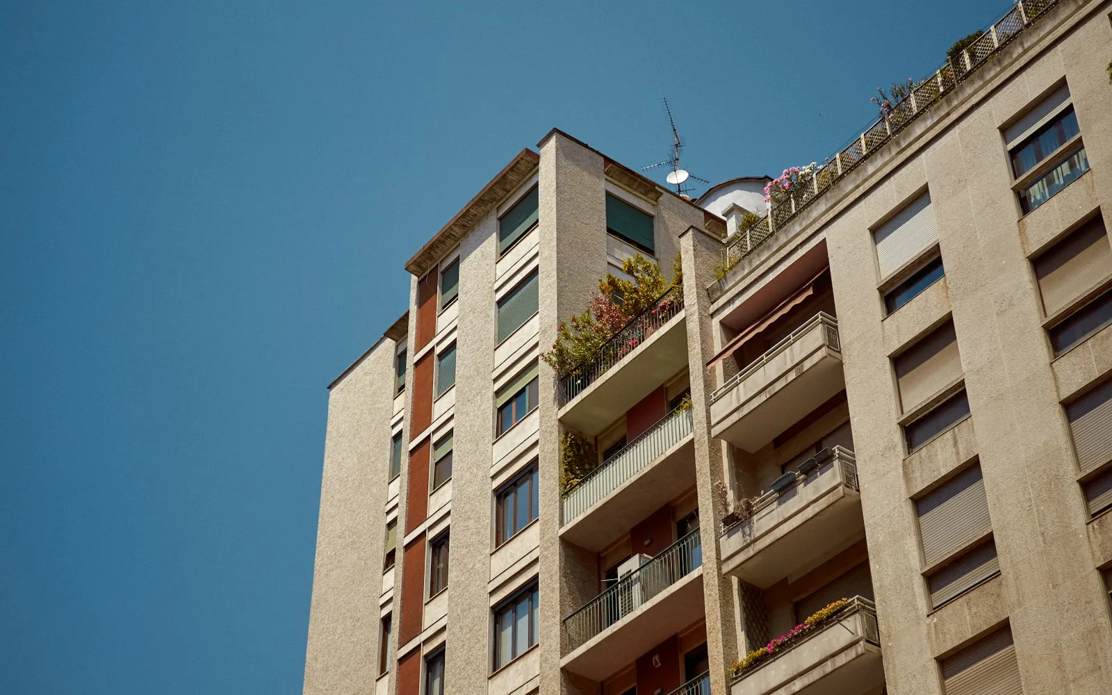 Palazzo residenziale milanese del dopoguerra con balconi fioriti e tapparelle.