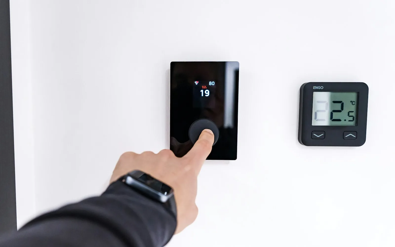 Mano che regola un termostato digitale a parete accanto a un display con la temperatura.