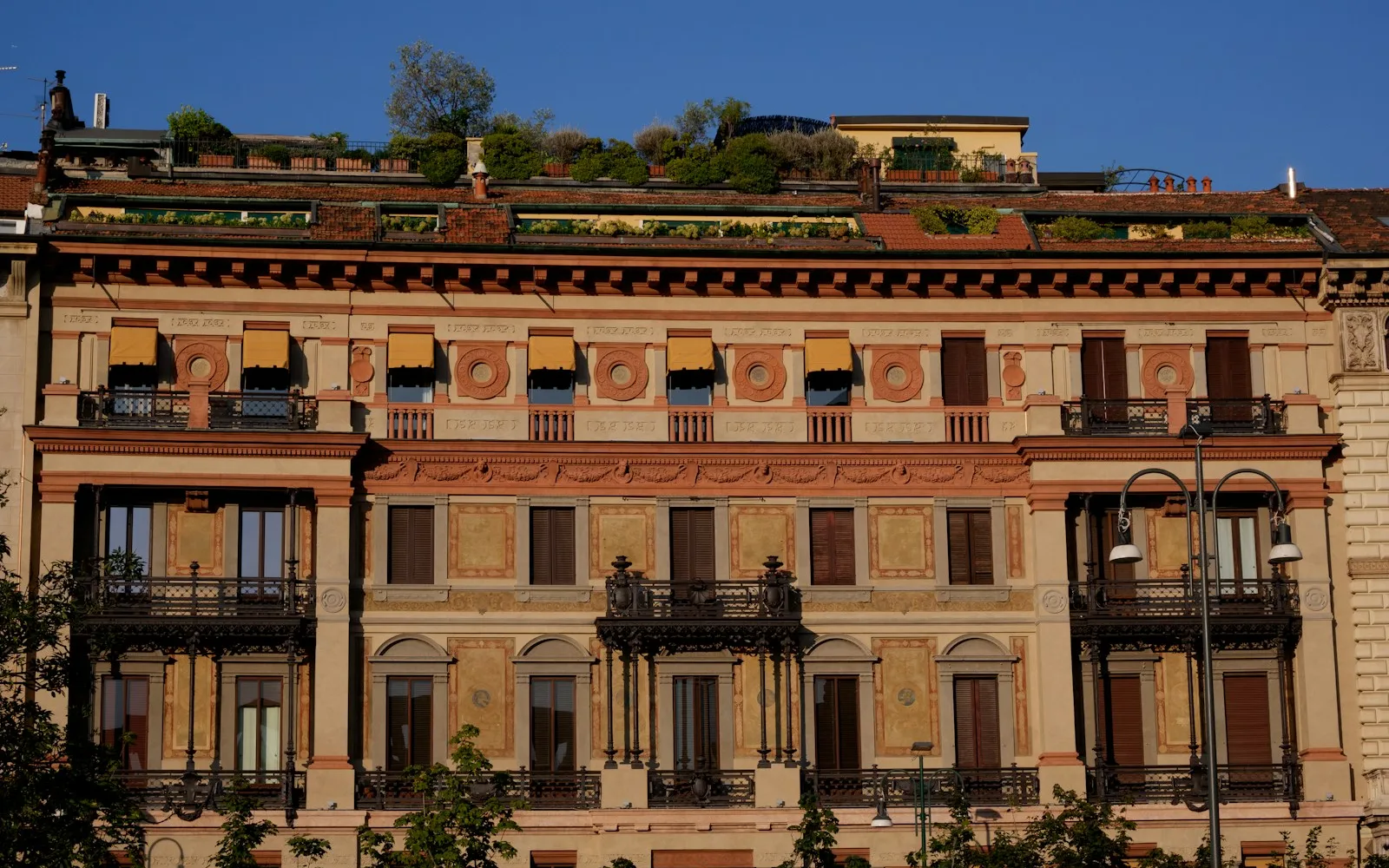 Facciata decorata di un palazzo residenziale italiano con balconi in ferro battuto e terrazzo verde in copertura.