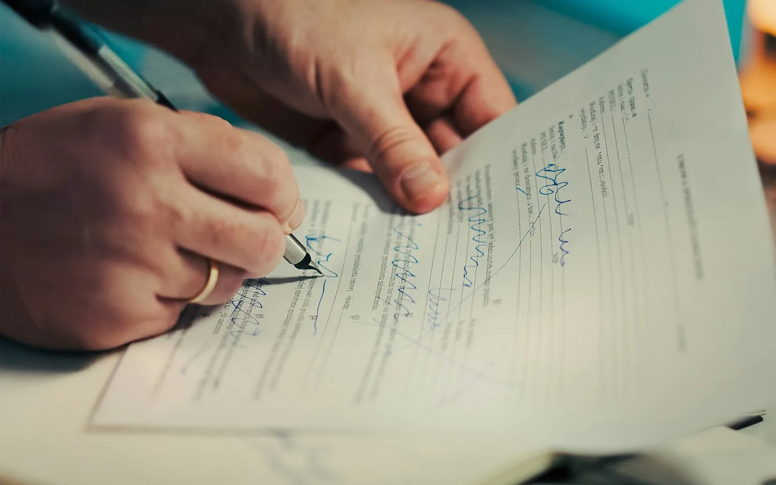 Due mani firmano un documento con una penna su una scrivania.