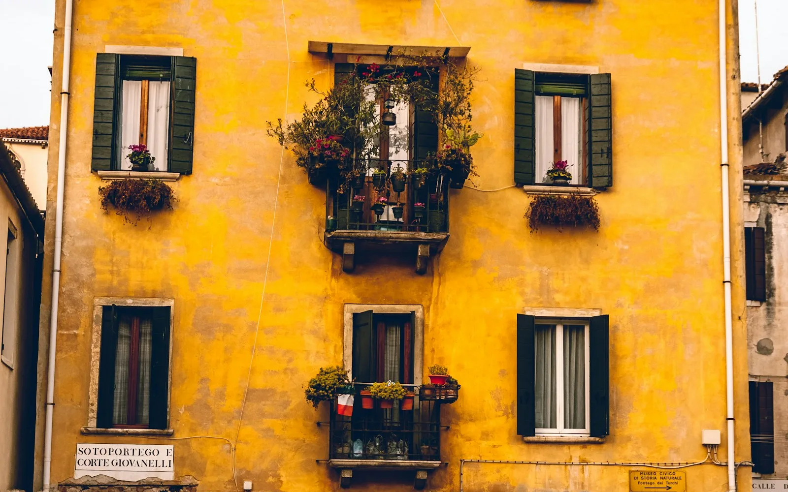 Piccolo palazzo giallo con persiane verdi e balconi fioriti a Venezia.