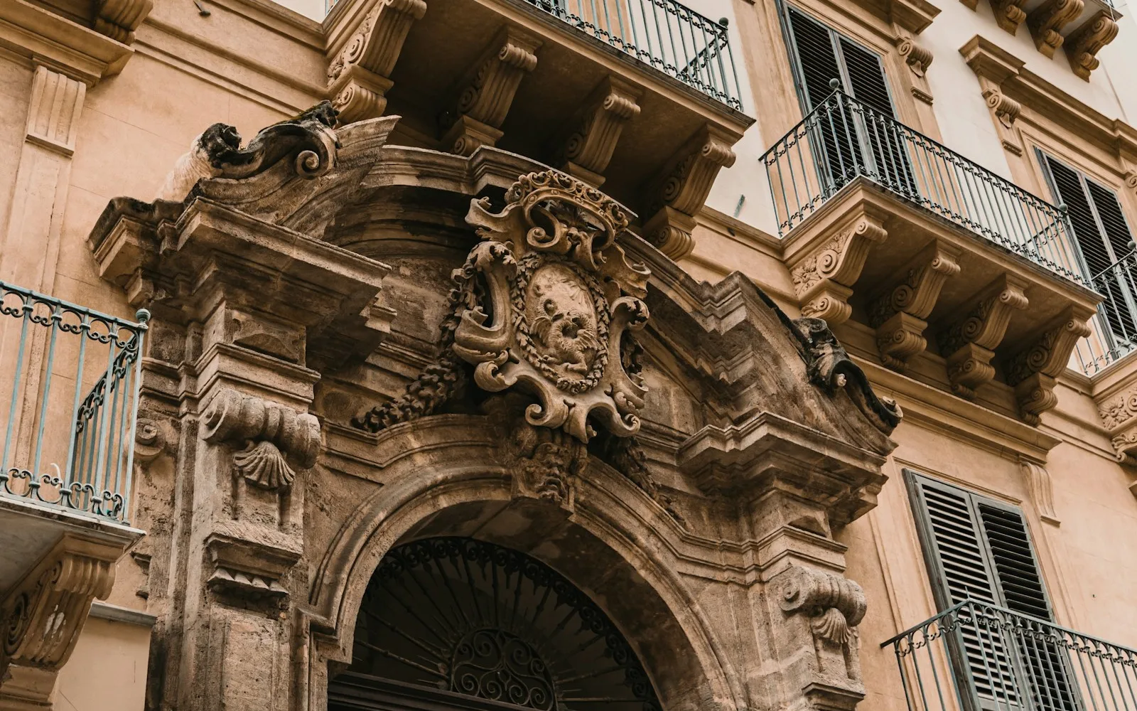 Portale barocco in pietra di un palazzo italiano con balconi e persiane ai piani superiori.