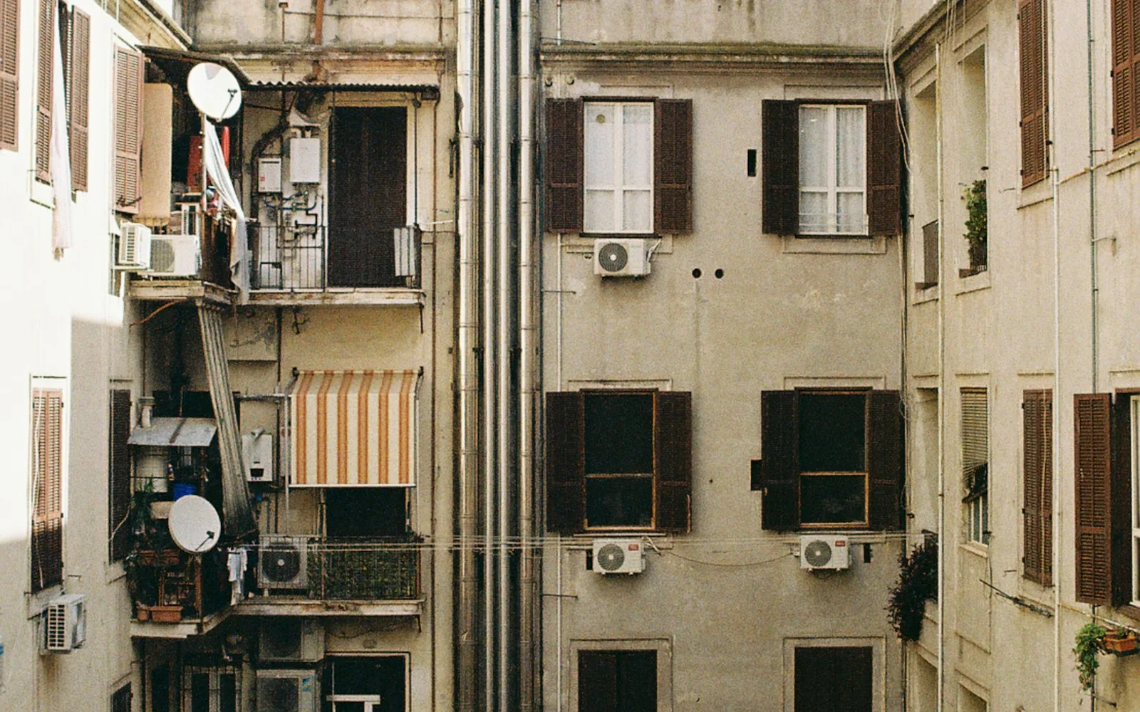 Cortile interno di un palazzo con persiane, condizionatori e canne fumarie.