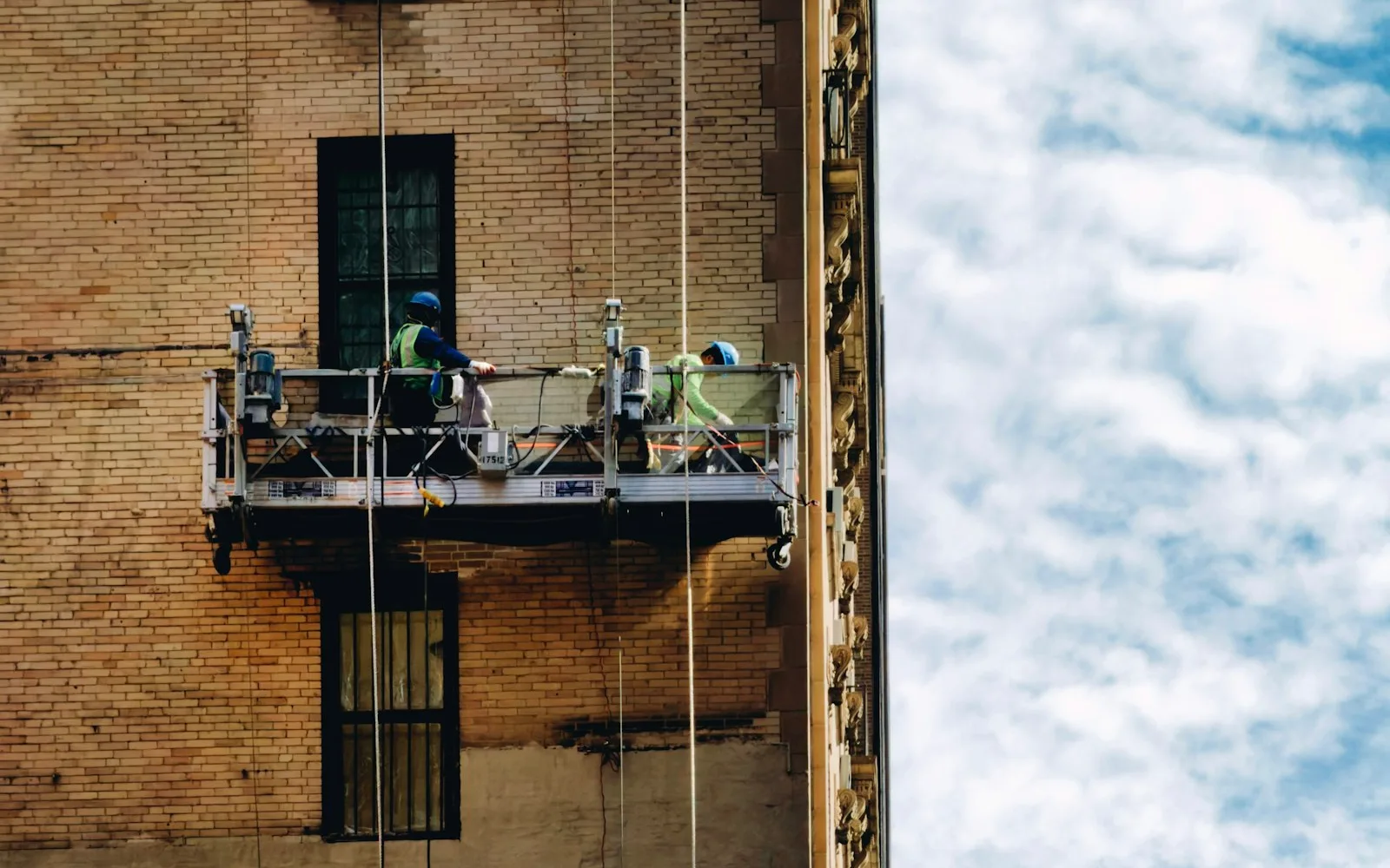 Operai su una piattaforma sospesa mentre lavorano sulla facciata di un edificio.