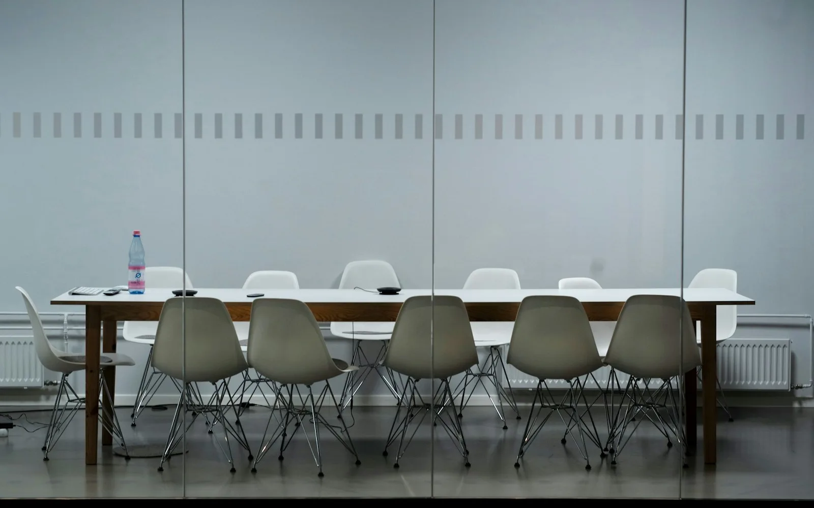 Sala riunioni con tavolo lungo e sedie, vista attraverso una vetrata.