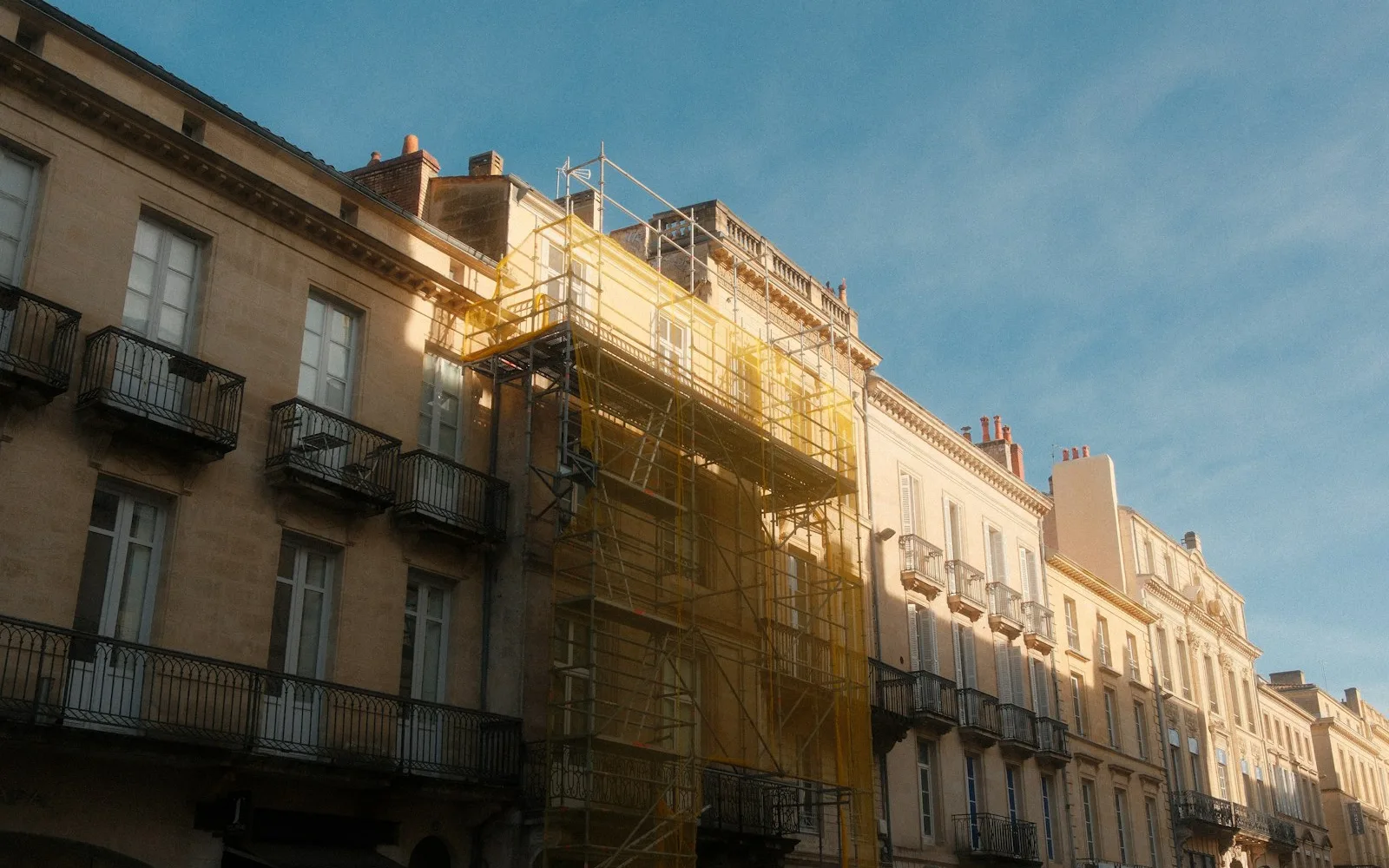 Ponteggio giallo montato sulla facciata di un palazzo residenziale d'epoca con balconi in ferro.