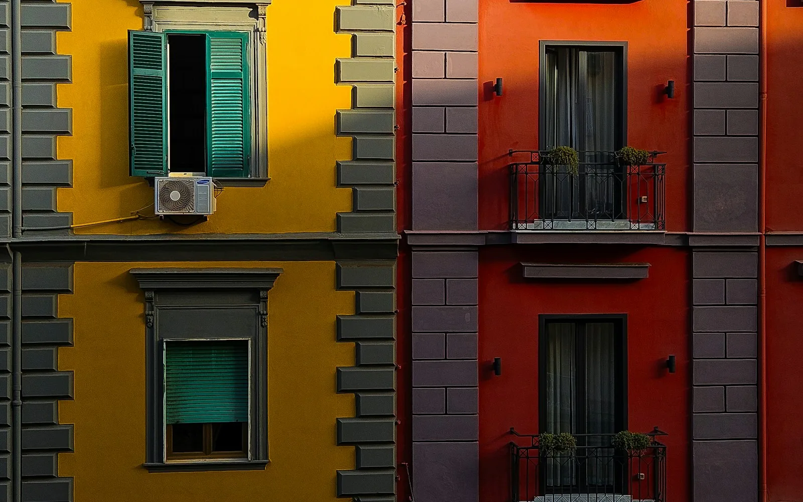 Due palazzi italiani adiacenti, uno giallo con persiane verdi e uno rosso con balconi.