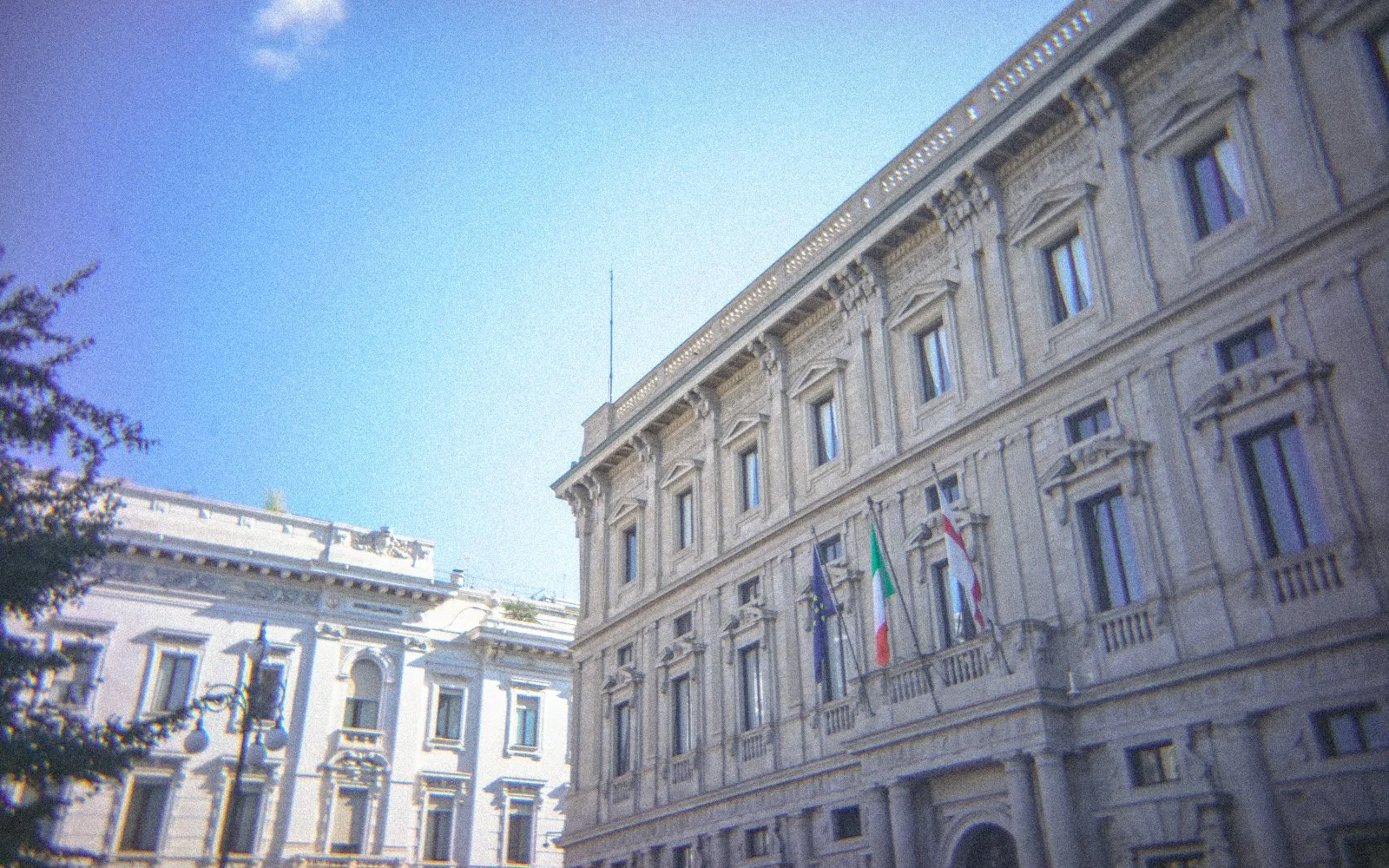 Palazzo istituzionale italiano in pietra con bandiere italiana, europea e cittadina sulla facciata.
