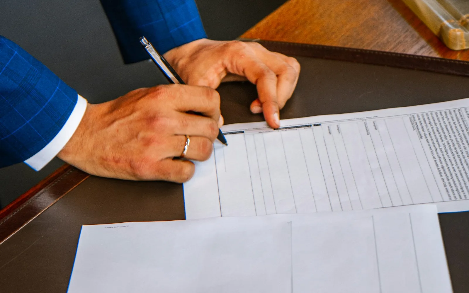 Mani che compilano un modulo con campi prestampati appoggiato su una scrivania di legno.