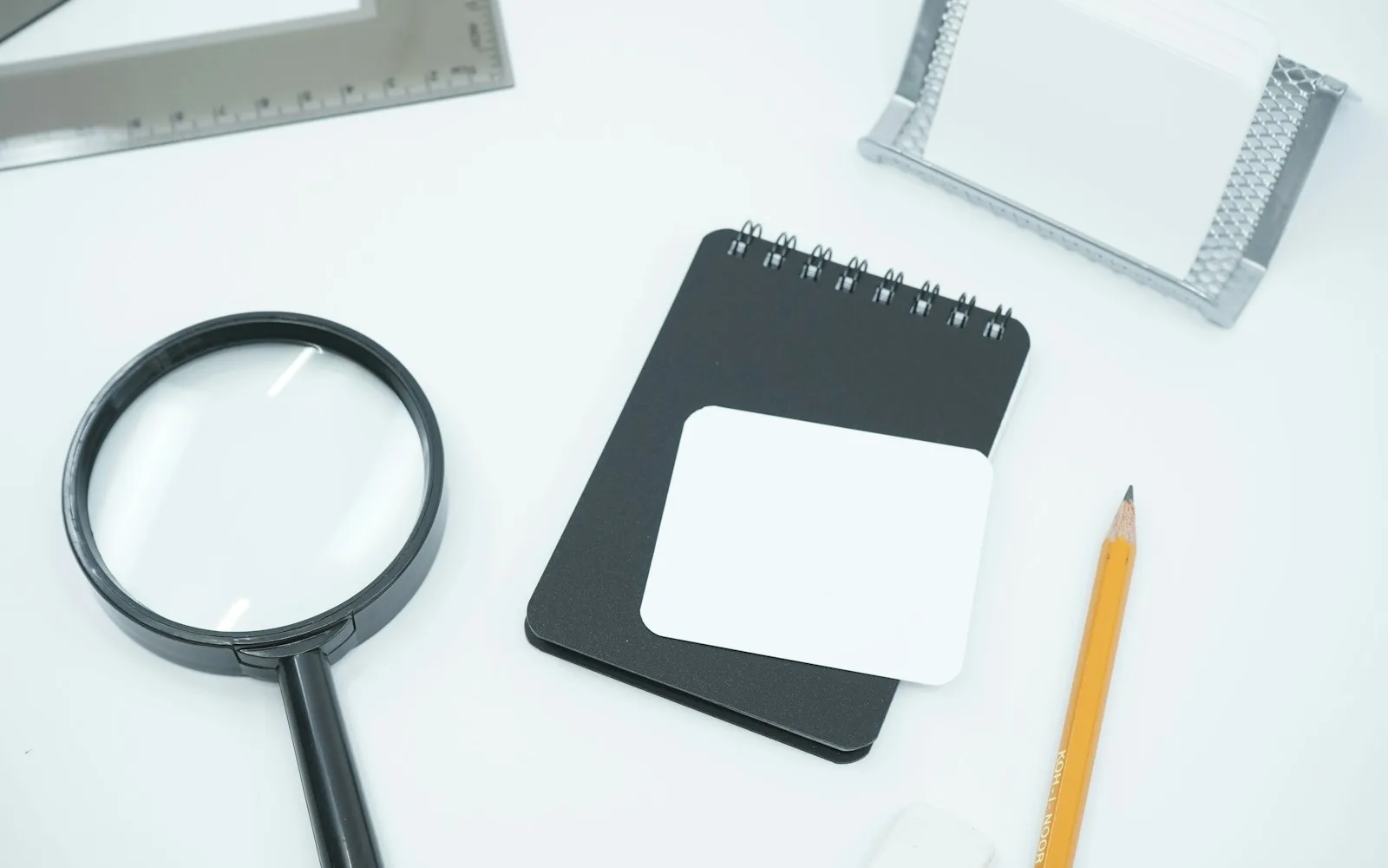 Lente d'ingrandimento accanto a un blocco per appunti e una matita su una scrivania.