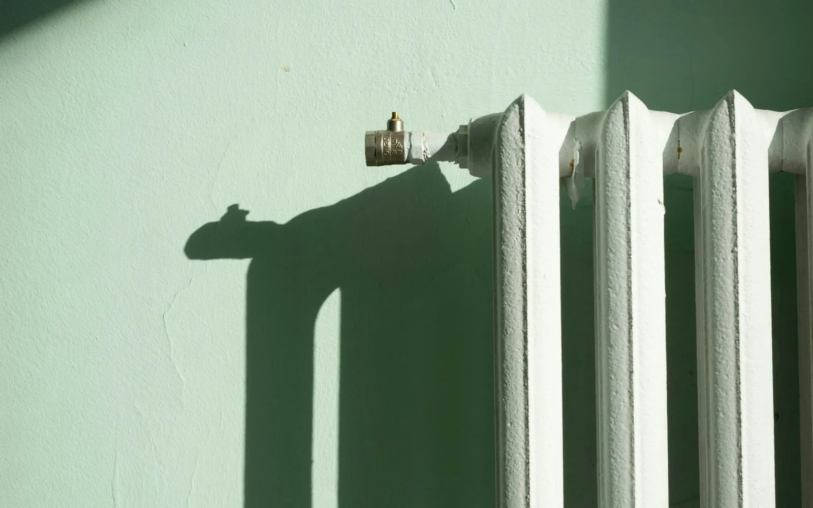 Termosifone bianco a parete in un appartamento, con la luce che disegna ombre.