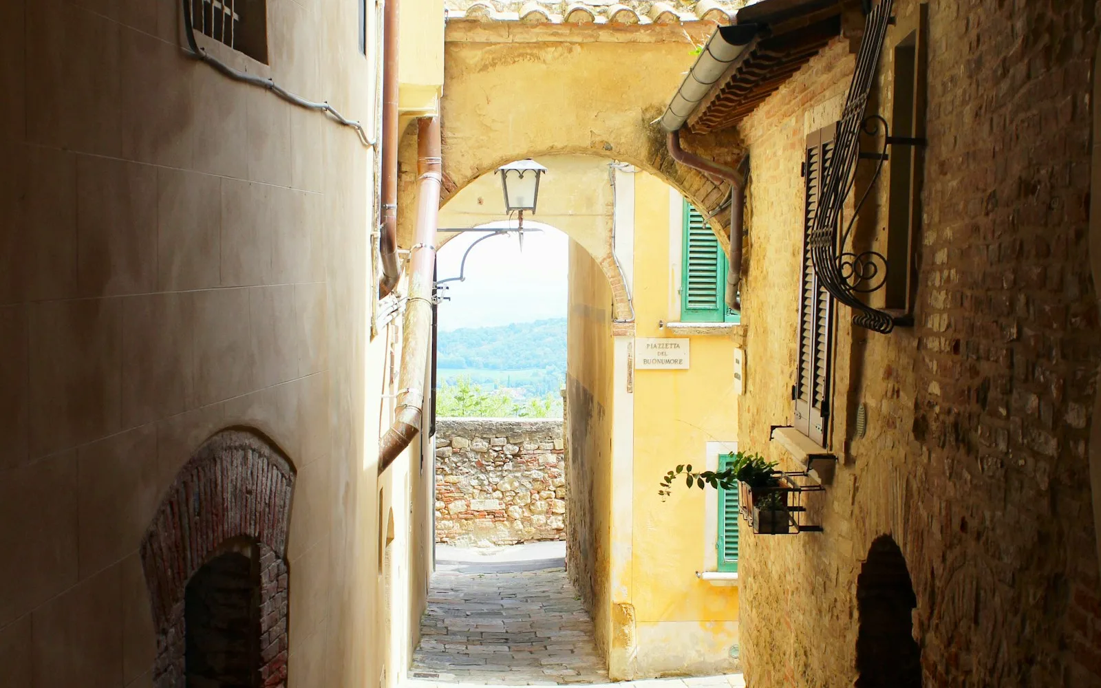 Vicolo italiano che passa sotto un arco tra due edifici con persiane verdi.