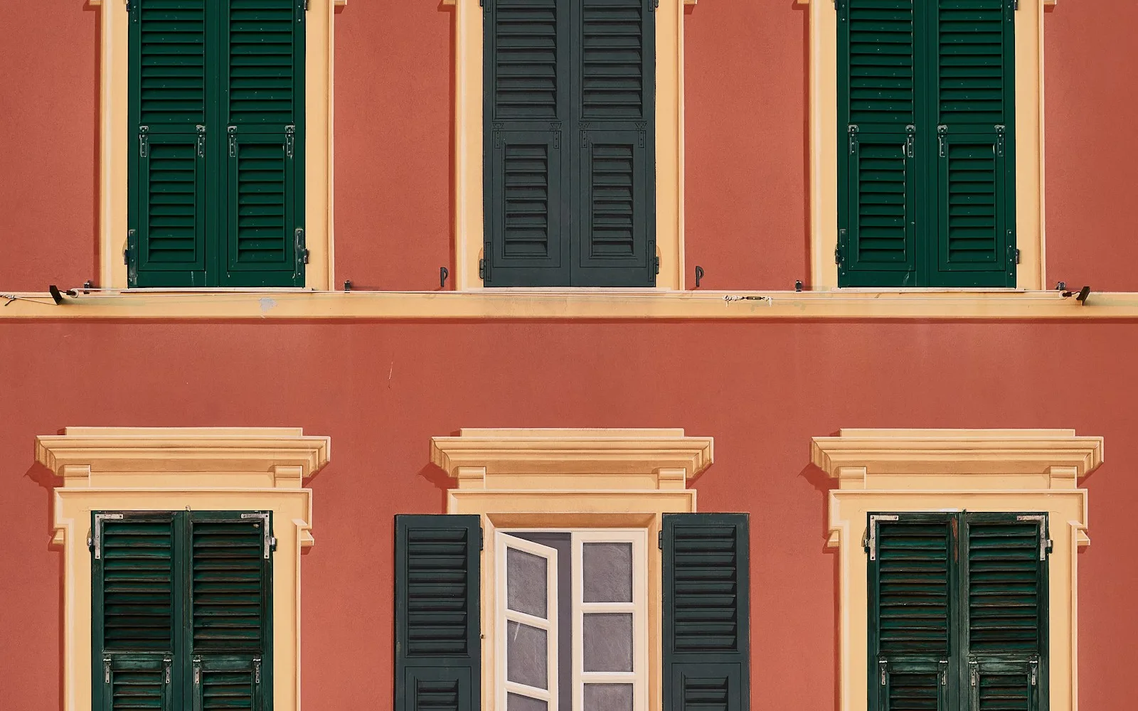 Facciata italiana color terracotta con persiane verdi quasi tutte chiuse.