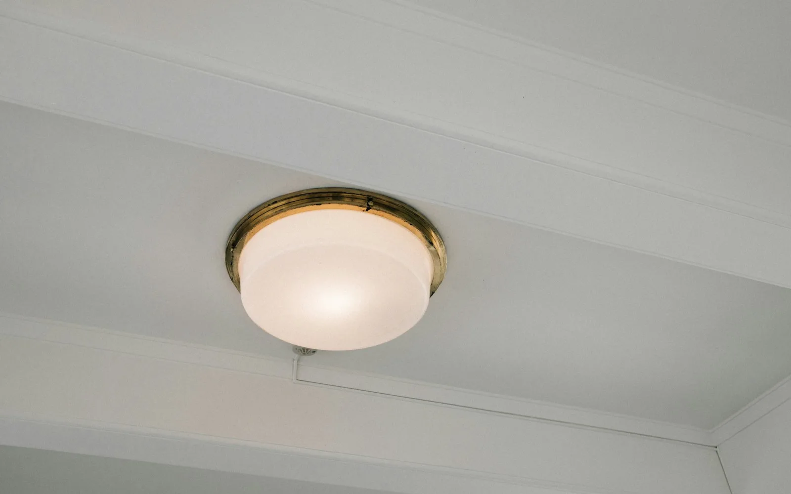 Soffitto intonacato di bianco con cornice e plafoniera in ottone, visto dal basso in un appartamento.