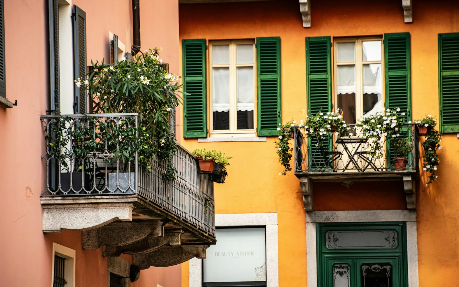 Palazzo italiano d'epoca con intonaco ocra e rosa, persiane verdi e balconi in ferro battuto fioriti.