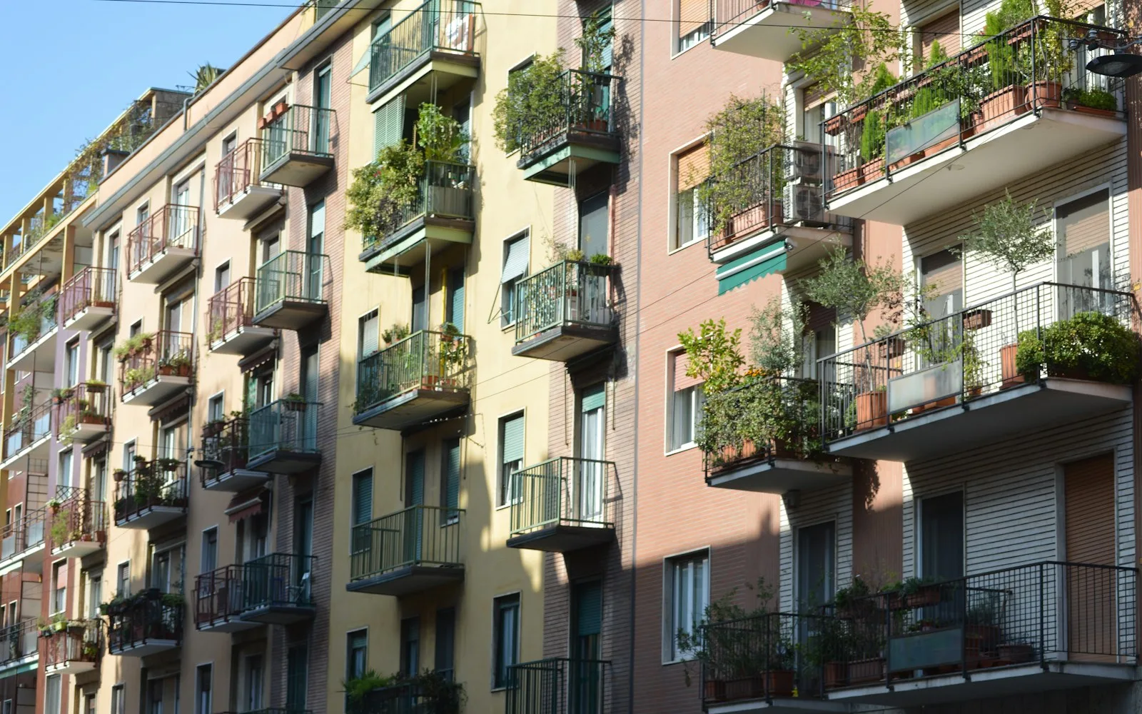 Facciate di più edifici residenziali contigui con balconi fioriti e tapparelle.